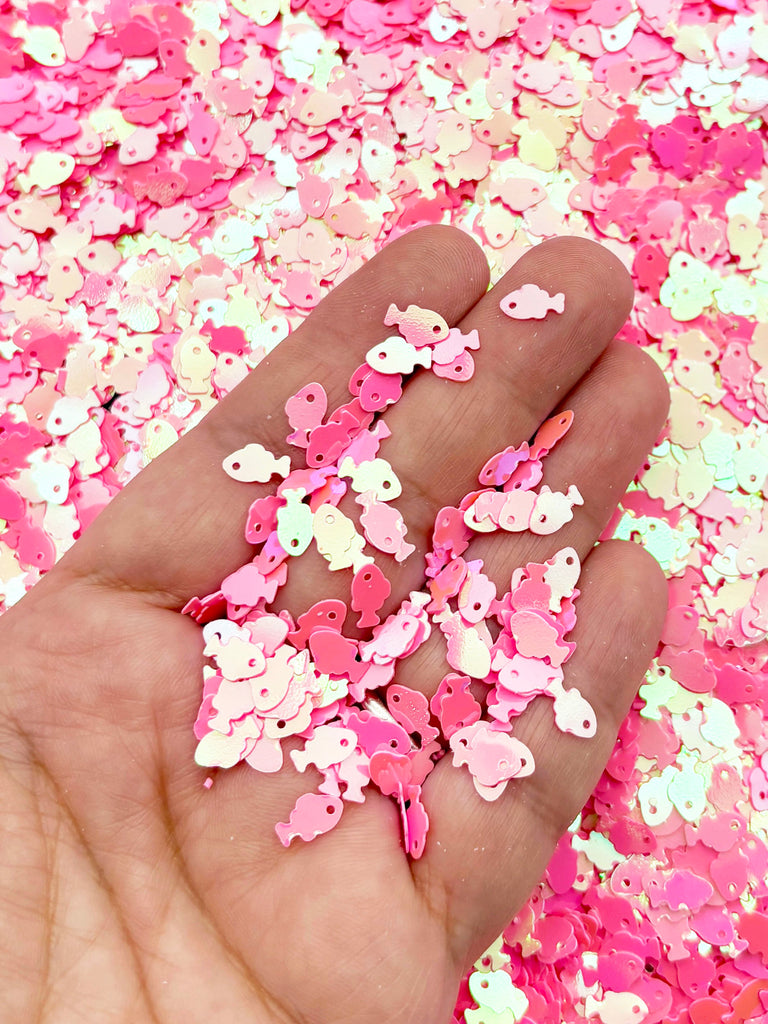 A hand holding a pile of pink and white sequin-like objects, creating a visually appealing and colorful display.