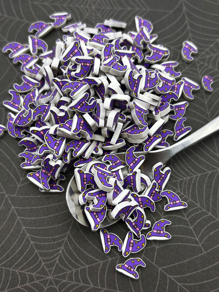 a pile of small purple and white wizard hat-shaped objects scattered on a dark surface, with a spoon visible in the background.