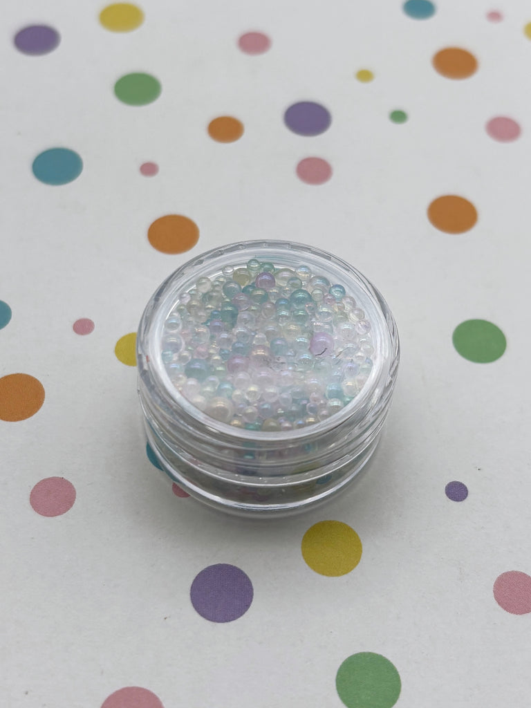 A clear container filled with multicolored beads is placed on a white surface with colorful polka dots.