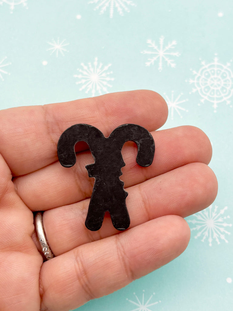 A hand holding a black candy cane-shaped object against a light blue background with white snowflakes.