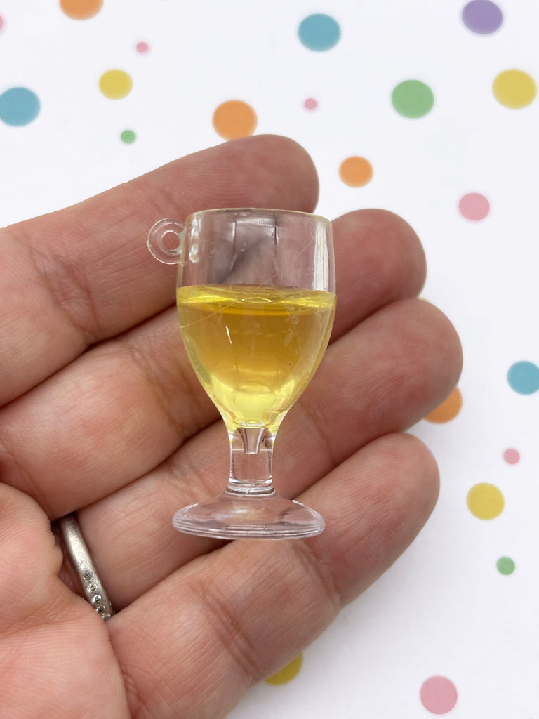 A hand holding a small glass of yellow liquid against a background with colorful polka dots.