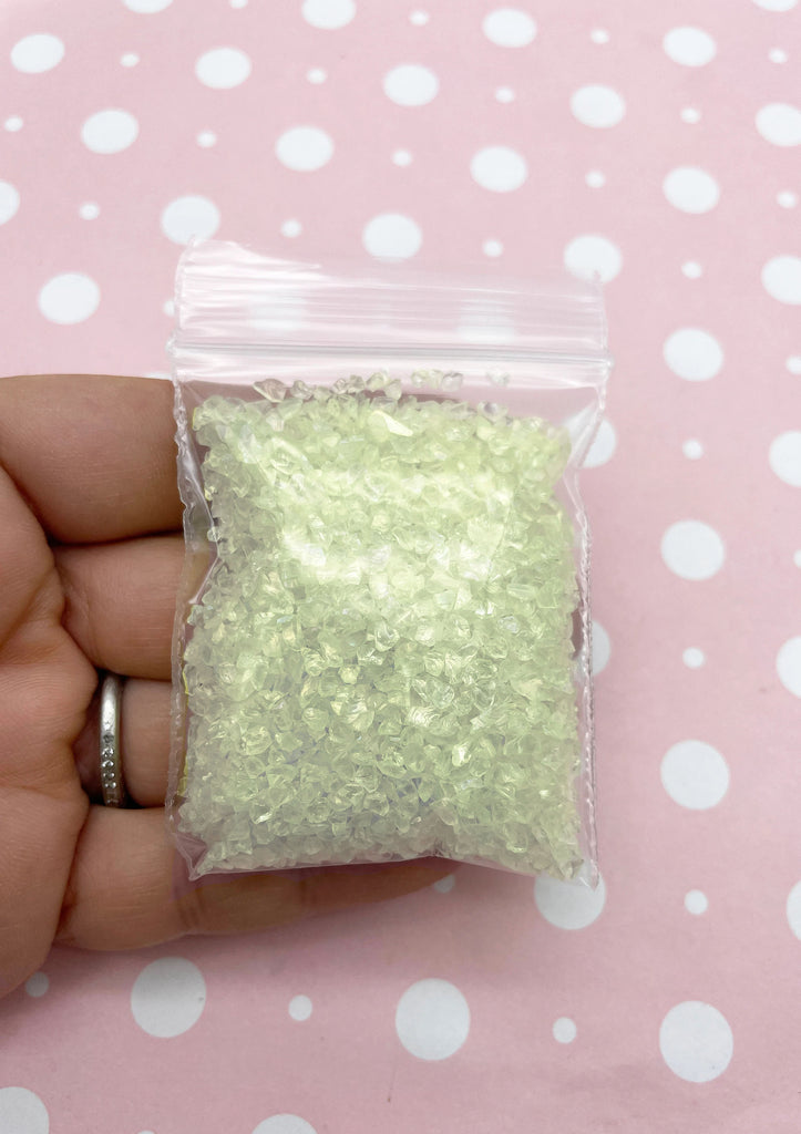 A hand holding a small bag filled with a pale green substance against a pink background with white polka dots.