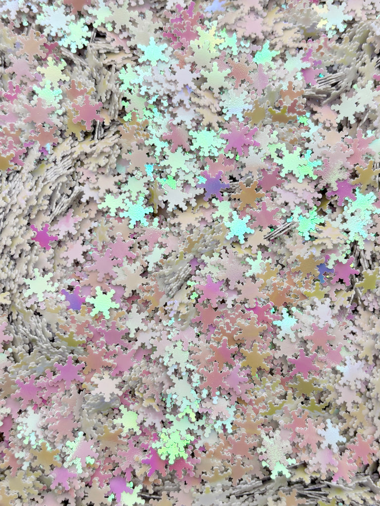 The image is a collage of various colored snowflakes, including pink, green, and white, scattered across a surface.