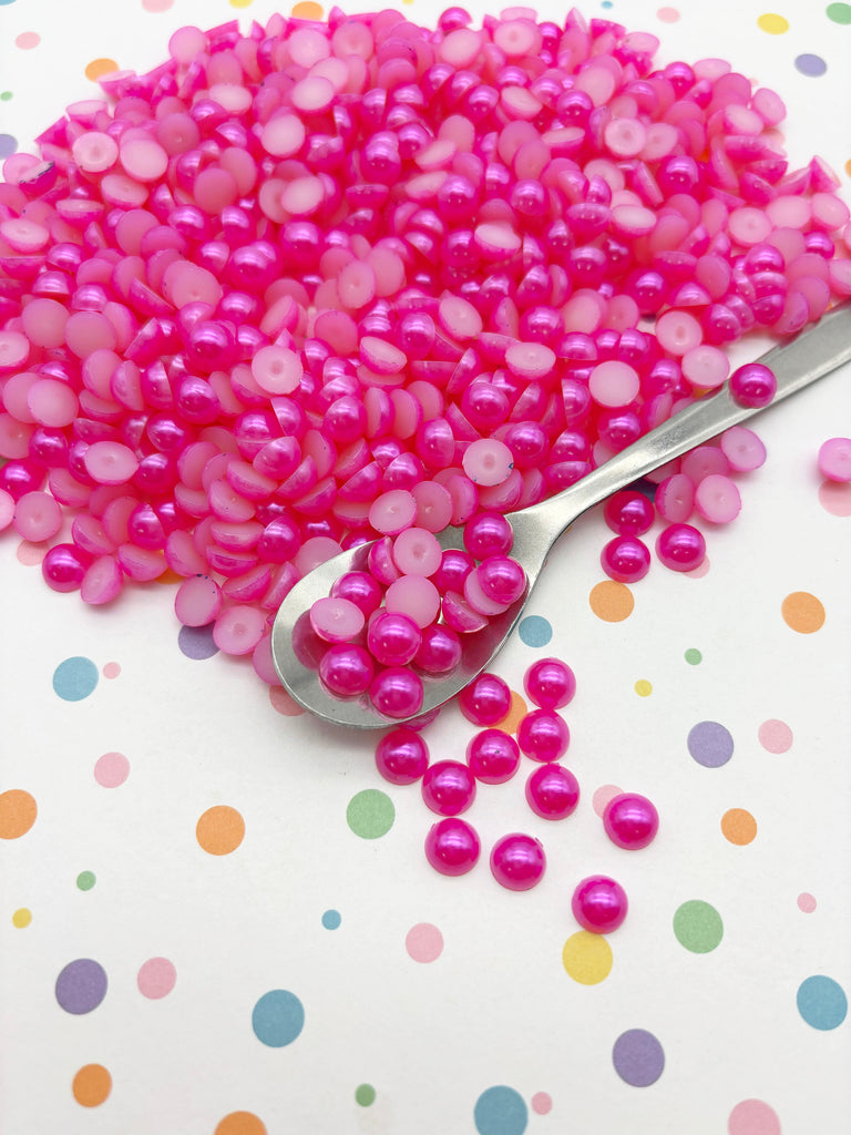 a pile of pink beads on a white background with colorful polka dots. A spoon is resting on the beads, and some of the beads are spilling out of the spoon onto the surface.