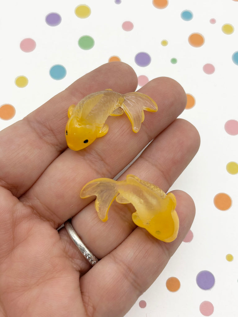 A hand holding two small, yellow fish-shaped objects against a background with colorful polka dots.