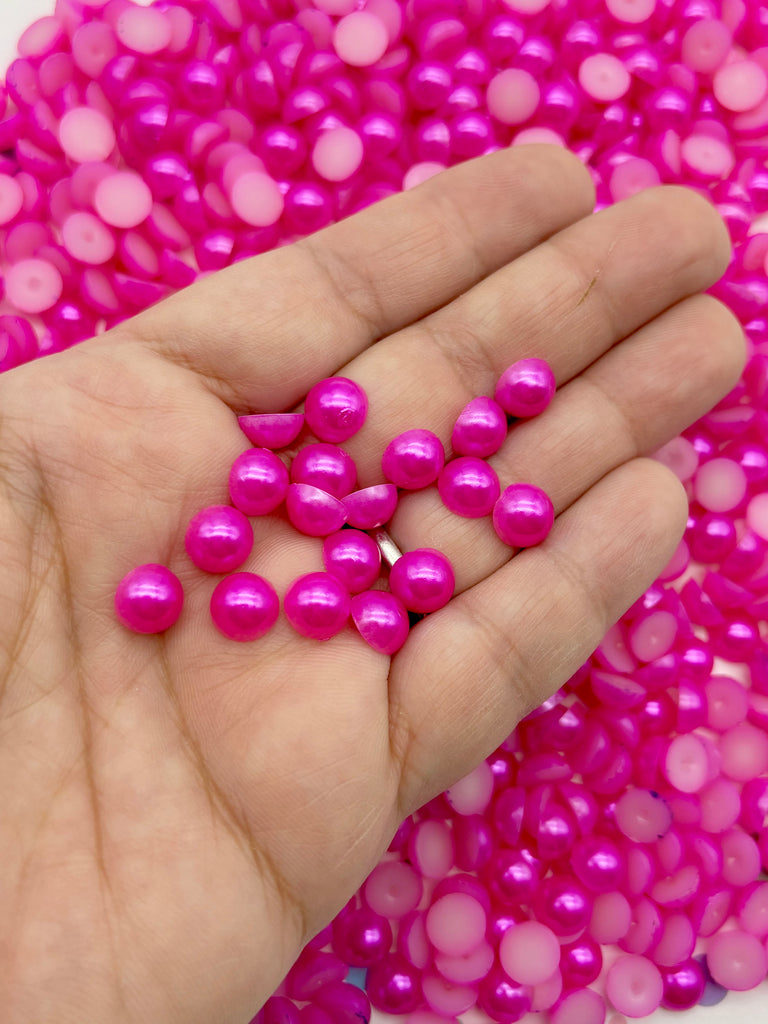 A hand holding a collection of small, shiny, pink beads against a background of similar pink beads.