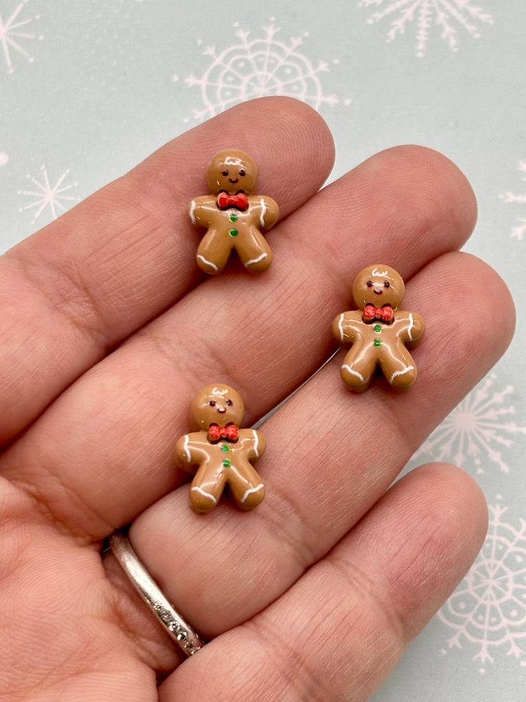 A hand holding three small gingerbread man figurines against a snowy background.