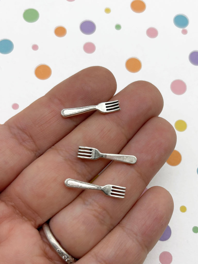 A hand holding three small silver forks against a background with colorful polka dots.