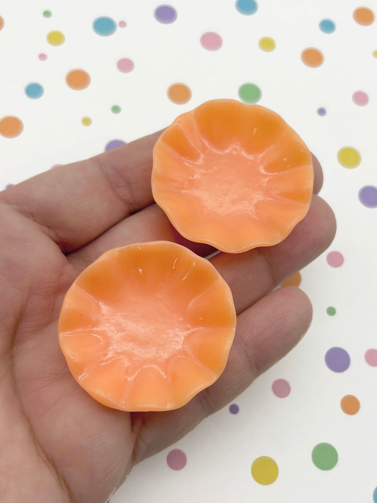 A hand holding two orange-colored flower-shaped objects against a background with colorful polka dots.