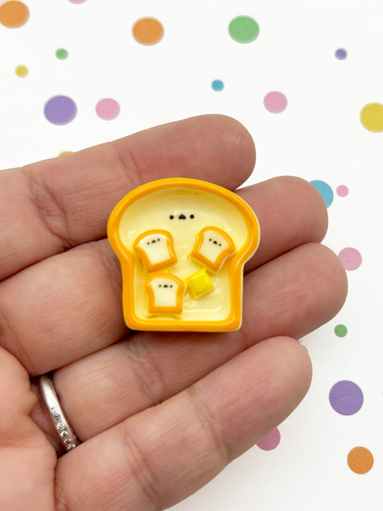 A hand holding a small yellow and orange object resembling a piece of toast with three small circles on it.