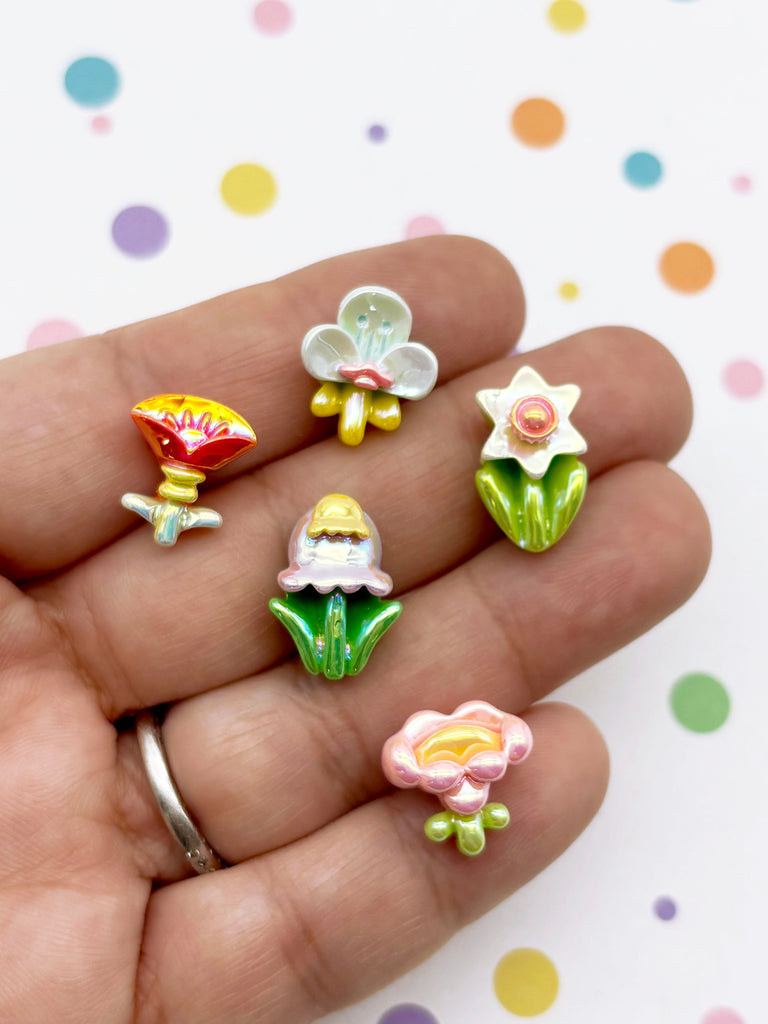 A hand holding five colorful, small flower-shaped charms against a background with polka dots.