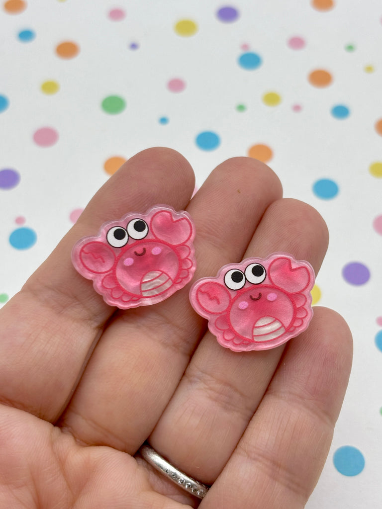 a hand holding two pink earrings with googly eyes