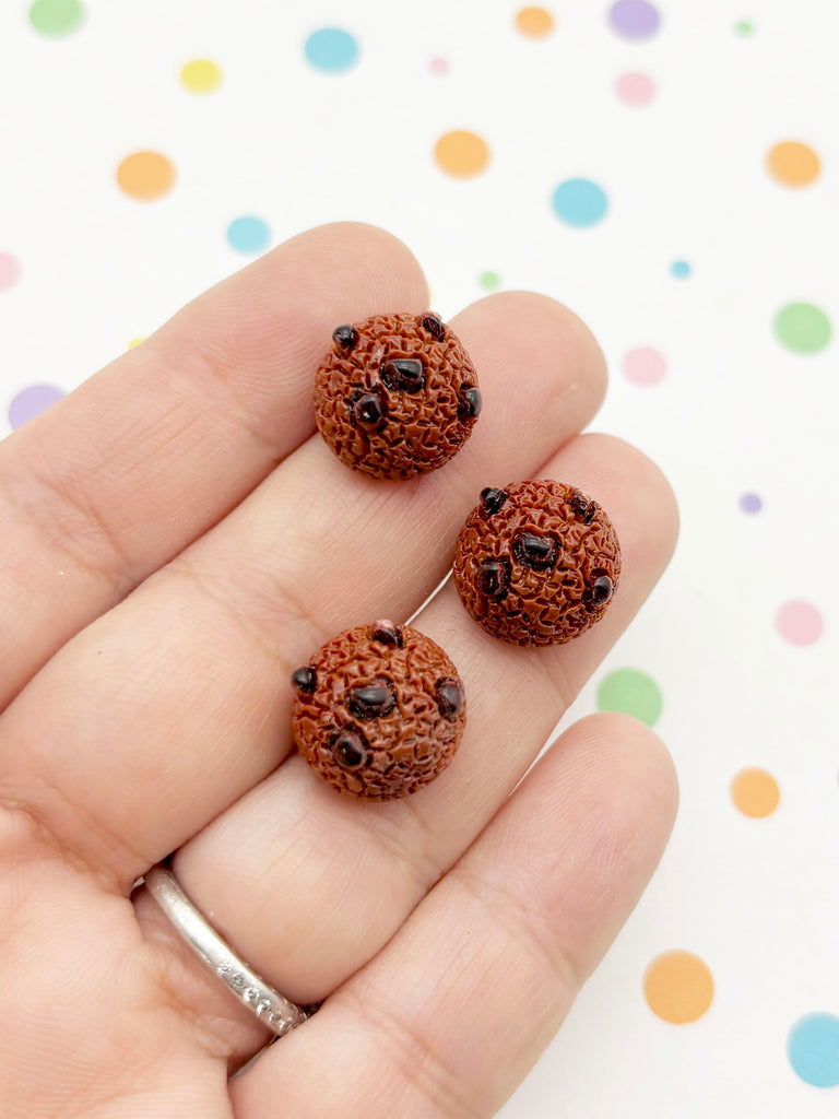 A hand holding three small, round chocolate chip cookies against a background with colorful polka dots.