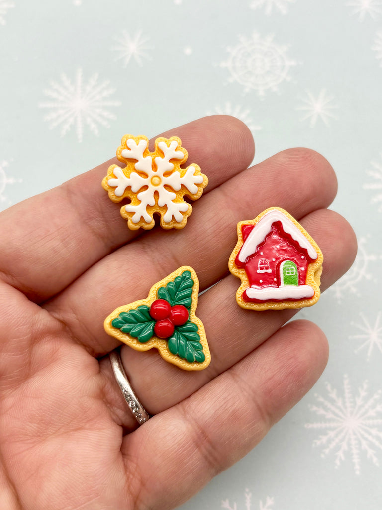A hand holding three small, festive-themed cookies against a snowy background.