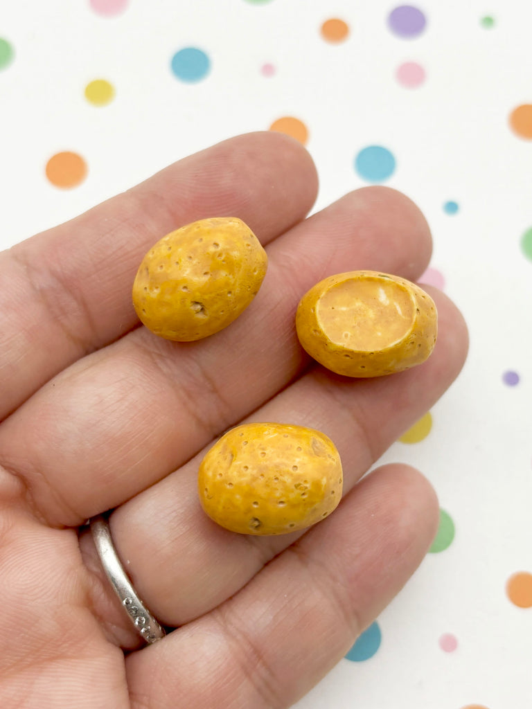 A hand holding three small, round yellow objects against a background with colorful polka dots.