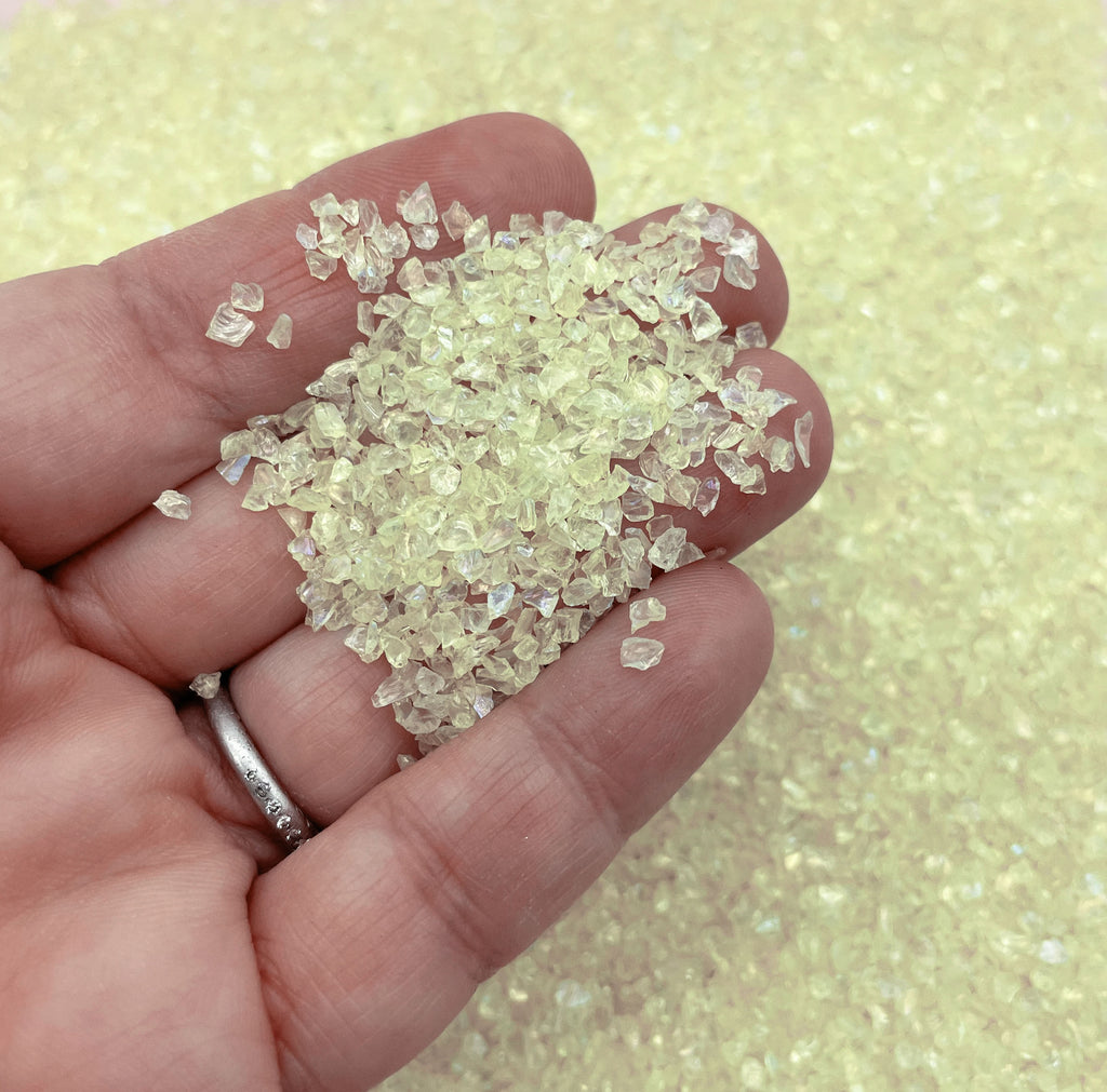 A hand holding a pile of small, clear, yellow-colored crystals or stones.