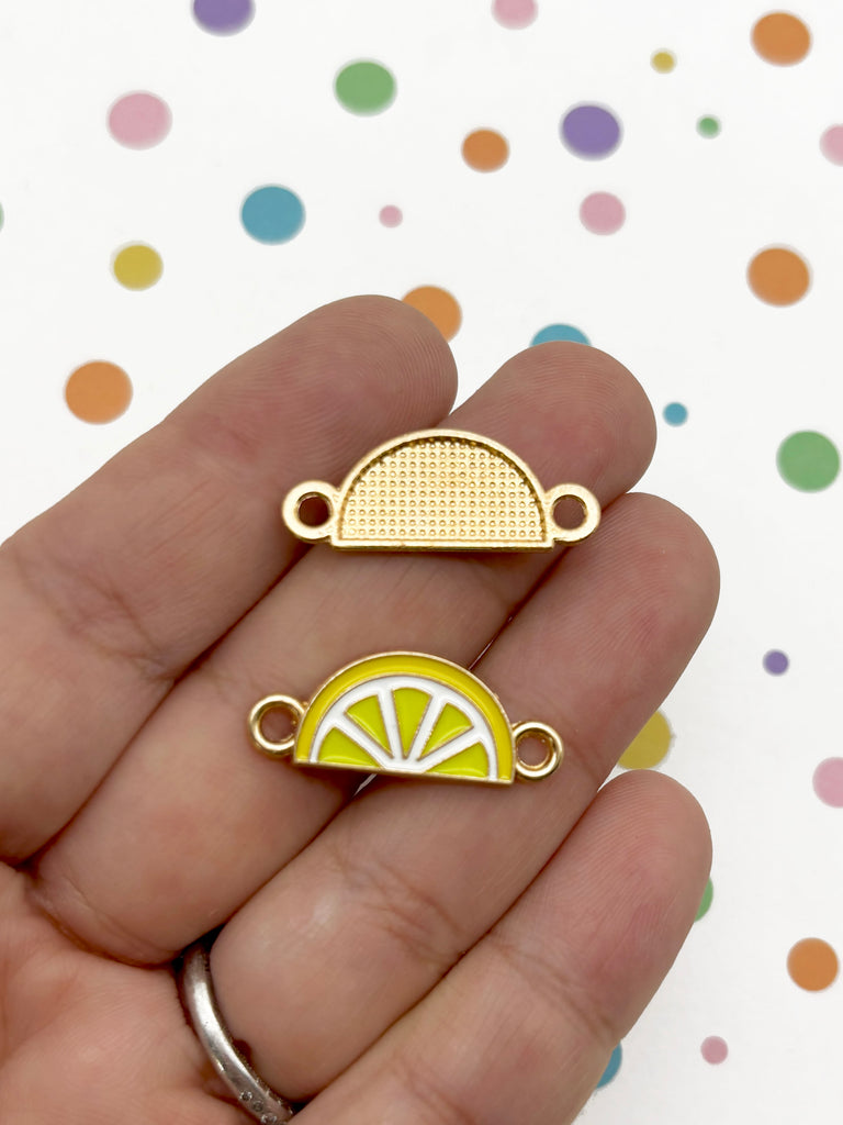 A hand holding two small, yellow and white enamel charms shaped like lemons against a background with colorful polka dots.