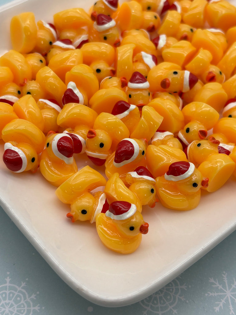 a white plate filled with numerous yellow rubber duckies wearing red Santa hats.