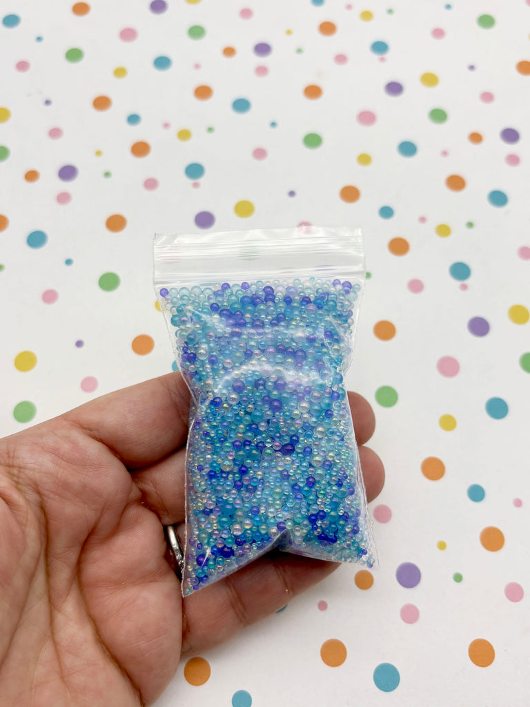 A hand is holding a small bag filled with blue and white beads against a background with colorful polka dots.