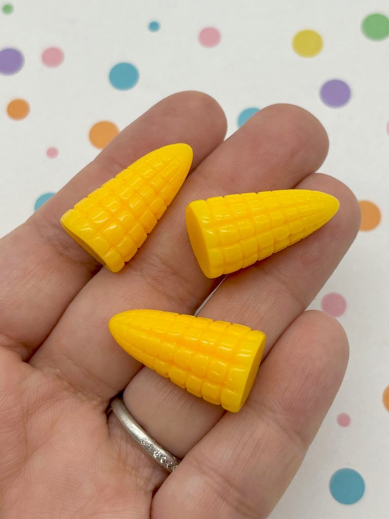 A hand holding three yellow plastic corn cob-shaped objects against a background with colorful polka dots.