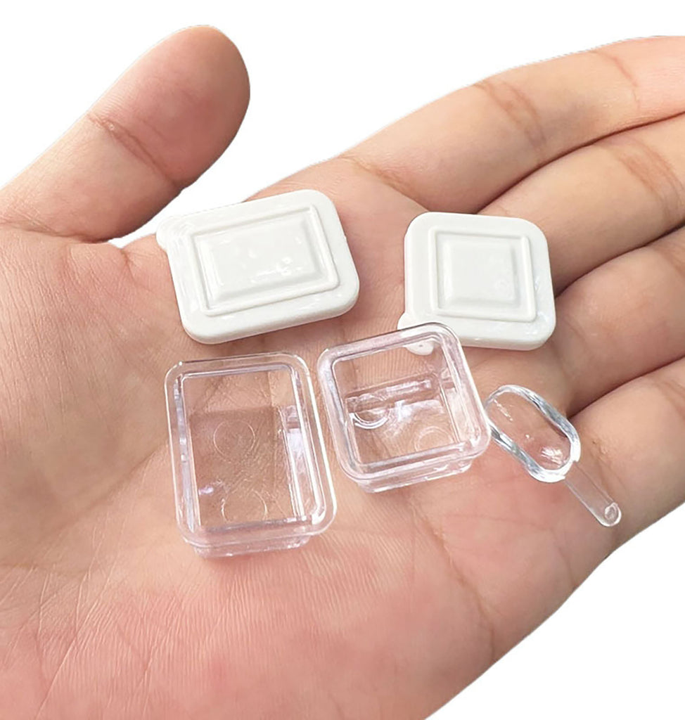 A hand holding two small white plastic containers with clear plastic lids.