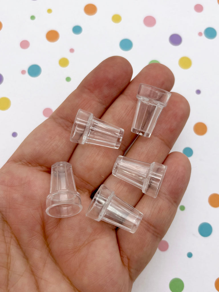 A hand holding five clear plastic cups against a background with colorful polka dots.