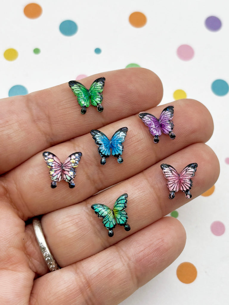 A hand holding a collection of colorful butterfly-shaped earrings against a background with polka dots.