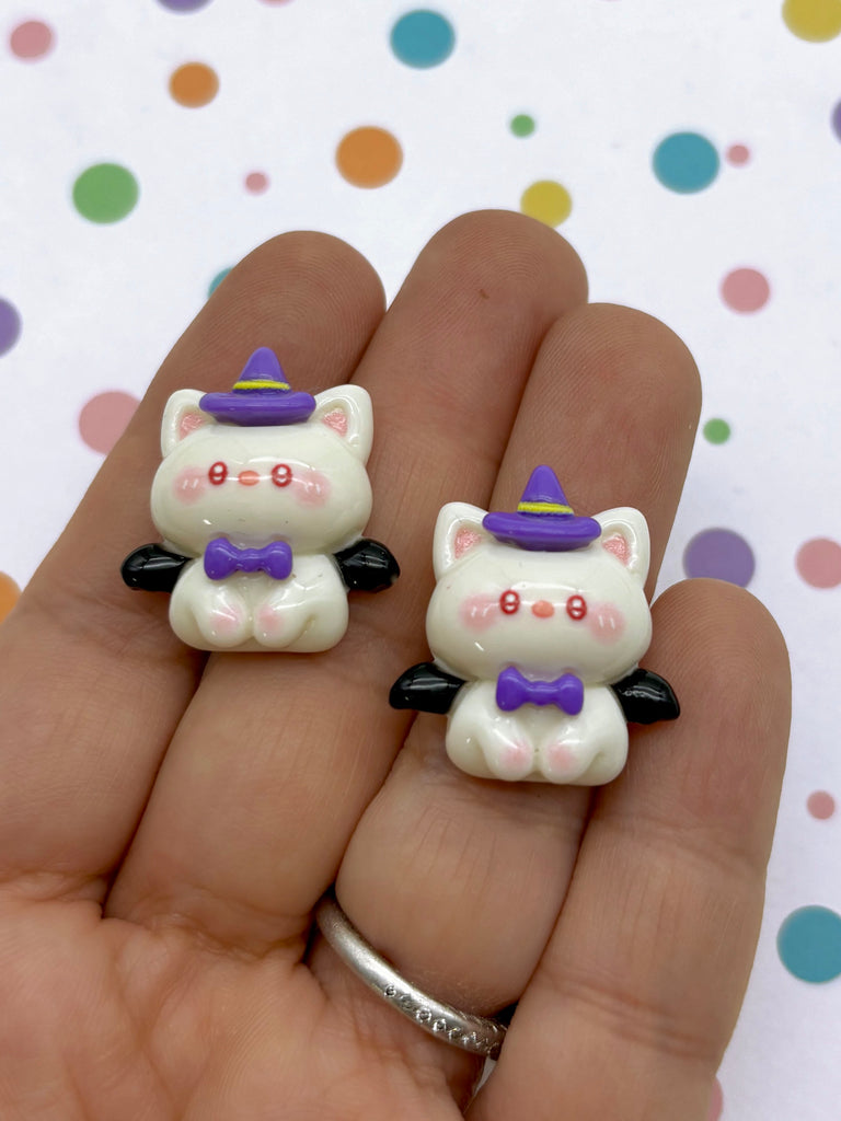 a hand holding two small white cat figurines