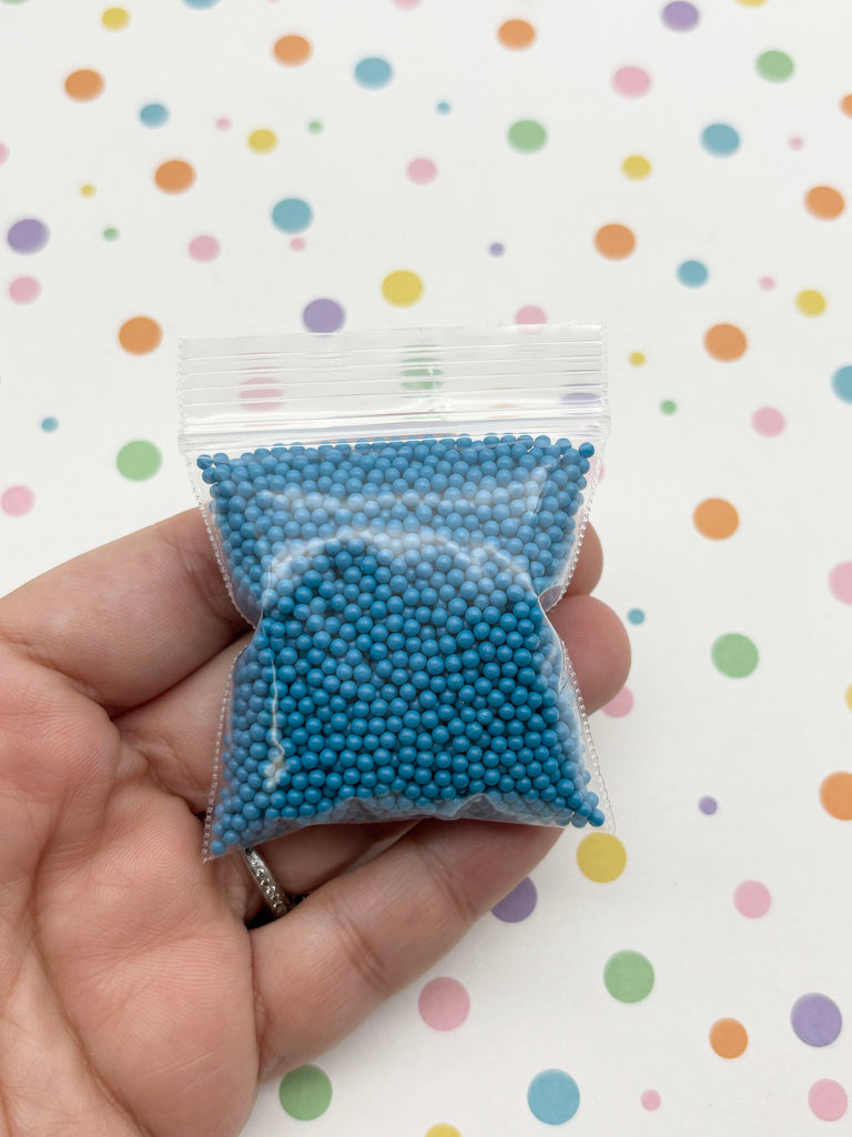 A hand is holding a small bag filled with blue beads against a background with colorful polka dots.
