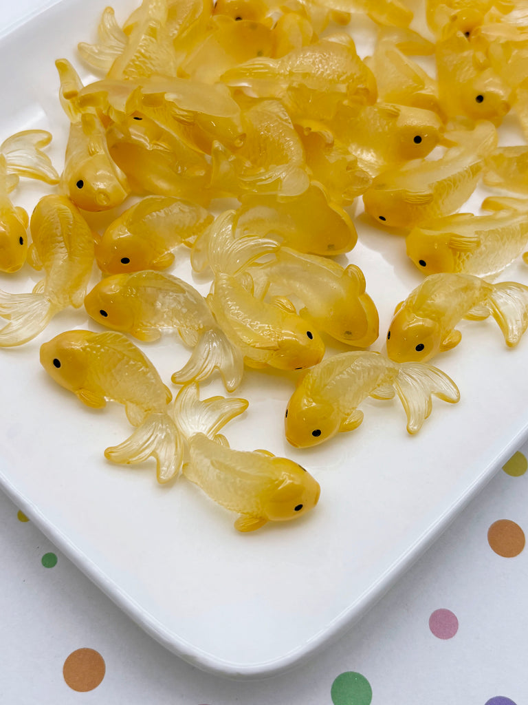 a white plate filled with numerous small, yellow fish-shaped objects, possibly made of plastic or glass.
