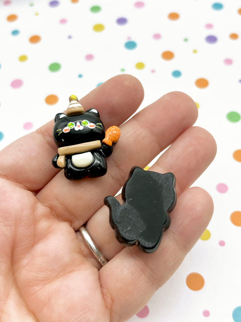 a hand holding a tiny black cat and a black cat brooch