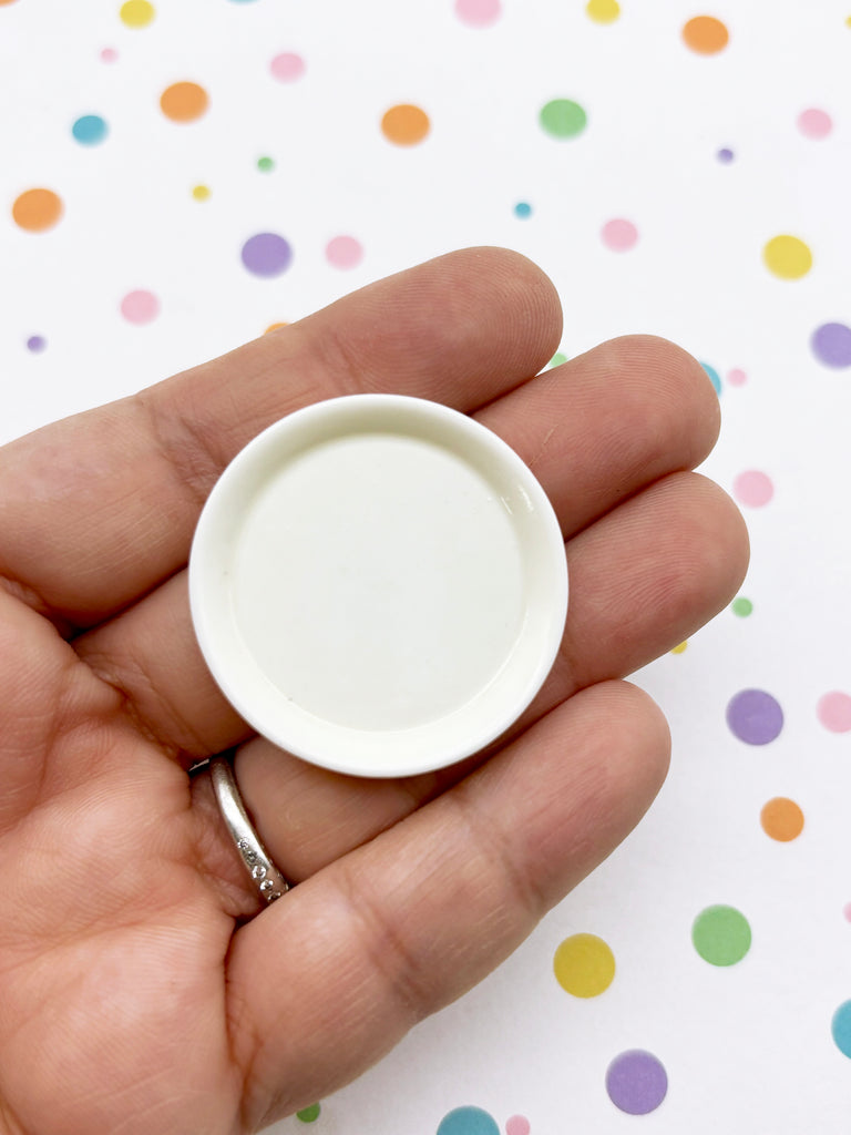 A hand holding a small white plate against a background with colorful polka dots.