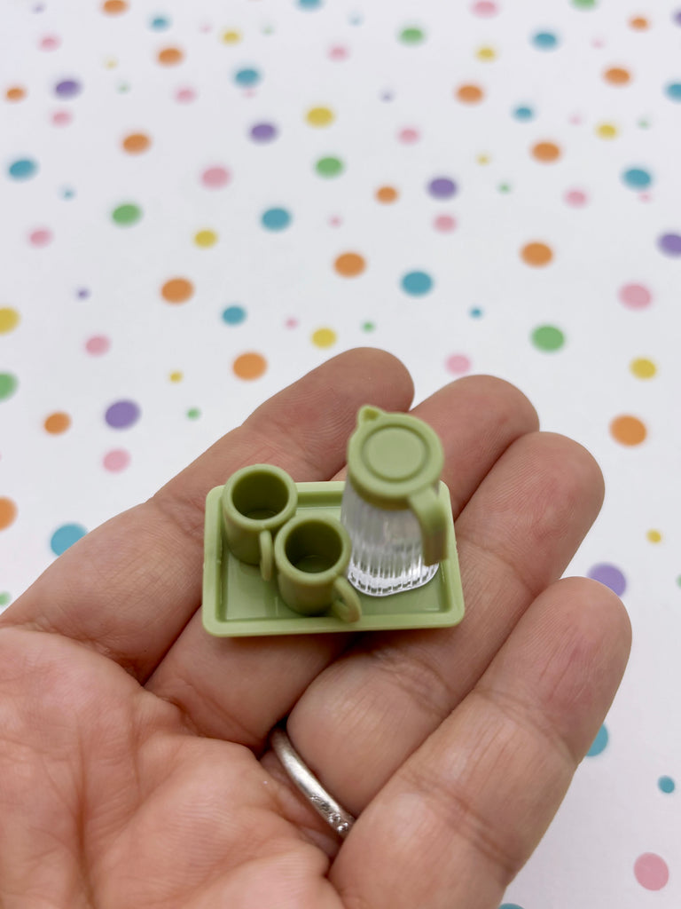 A hand holding a small green tray with two cups on it against a background with colorful polka dots.