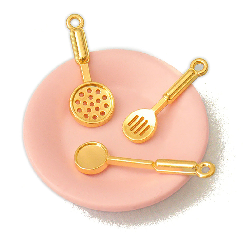 three gold-colored kitchen utensils, including a ladle, a spatula, and a ladle, arranged on a pink plate.
