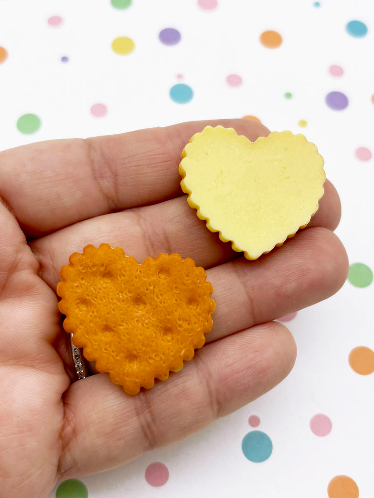 A hand holding two heart-shaped crackers, one orange and one yellow, against a background of colorful polka dots.
