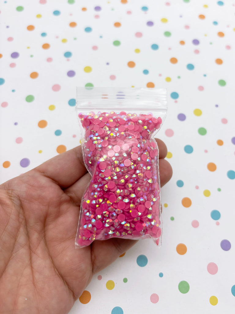 A hand is holding a small bag filled with pink glitter beads against a background with colorful polka dots.
