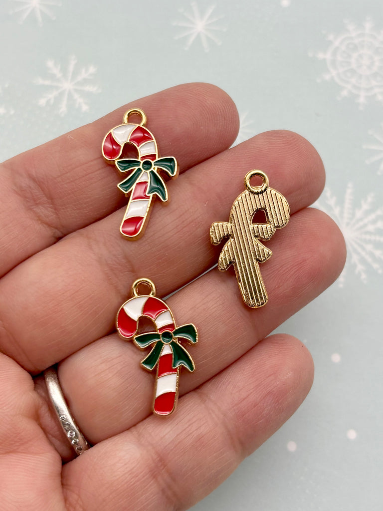 A hand holding three small Christmas-themed charms, including a candy cane, a gingerbread man, and a gingerbread man.