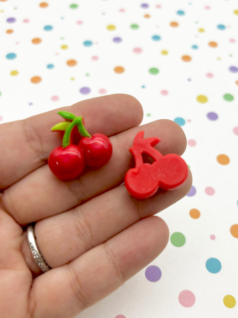 a hand holding a tiny cherry and a cherry shaped brooch