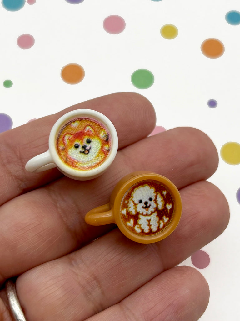 A hand holding two small coffee cups with cartoon animal faces on them.