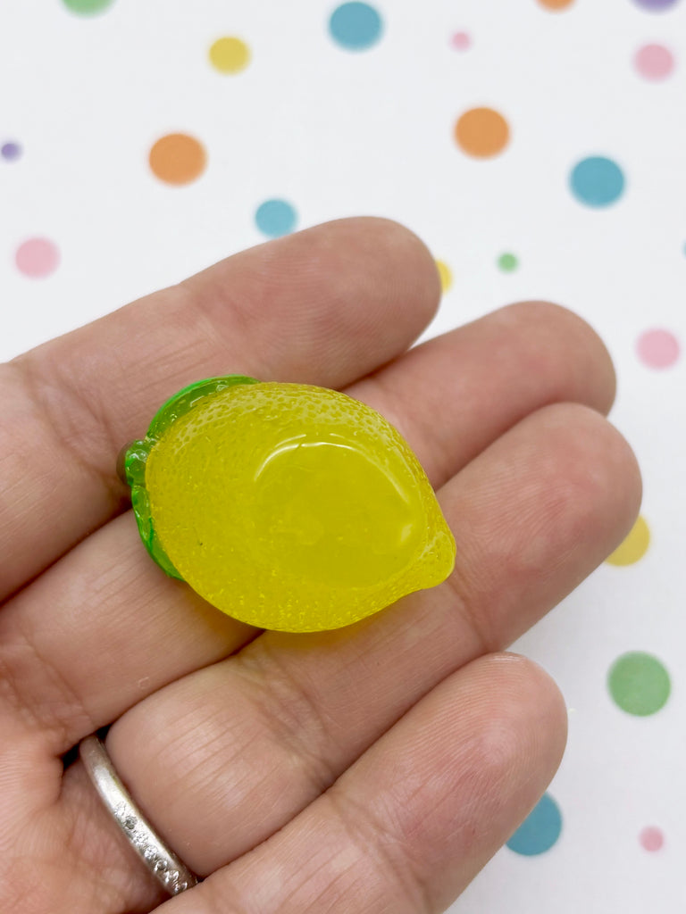 A hand holding a small, yellow, and green gummy lemon-shaped object against a background with colorful polka dots.
