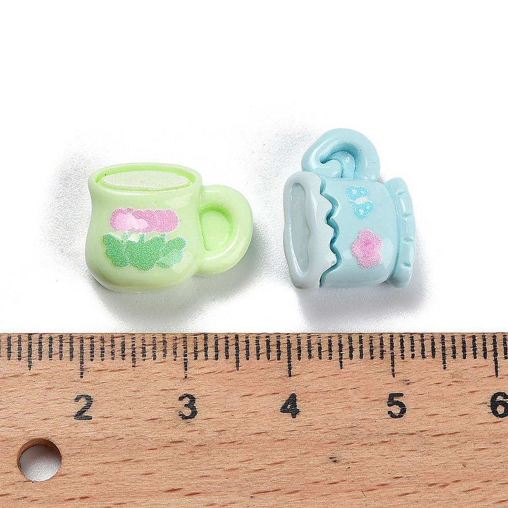 Two small toy mugs are placed next to a ruler for size comparison.