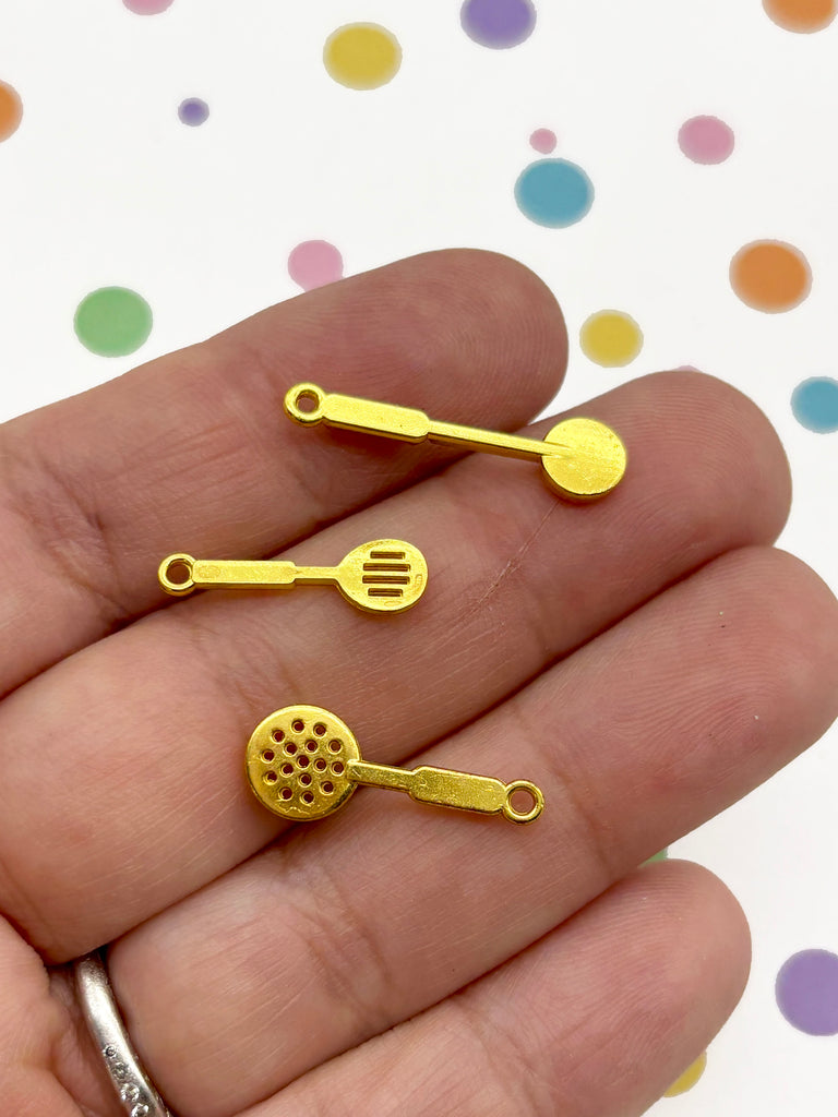 A hand holding three small, gold-colored spoons against a background with colorful polka dots.