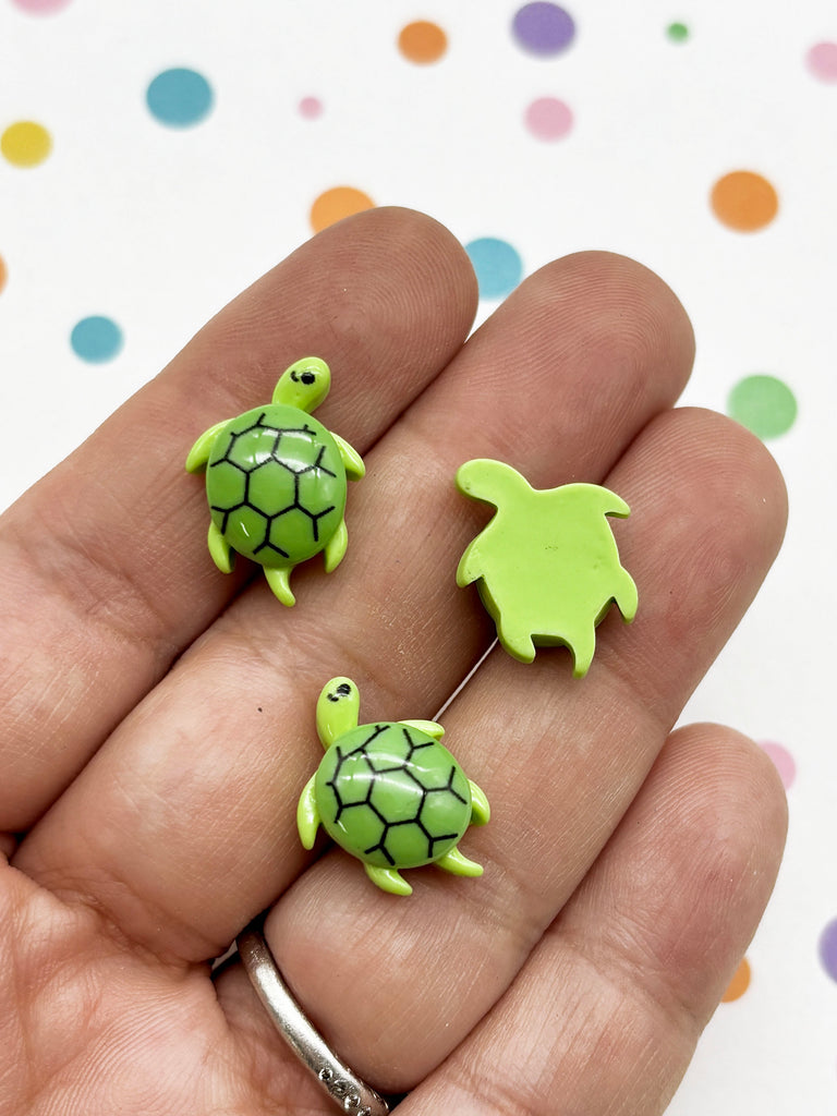 A hand holding three green turtle-shaped objects against a background with colorful polka dots.