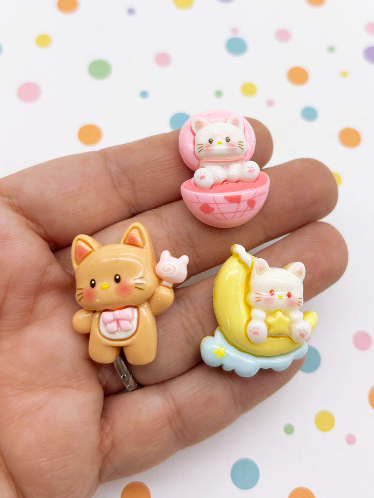 A hand holding three small, colorful figurines of cats.