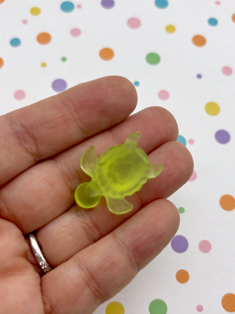 A hand holding a small, green turtle-shaped object against a background with colorful polka dots.