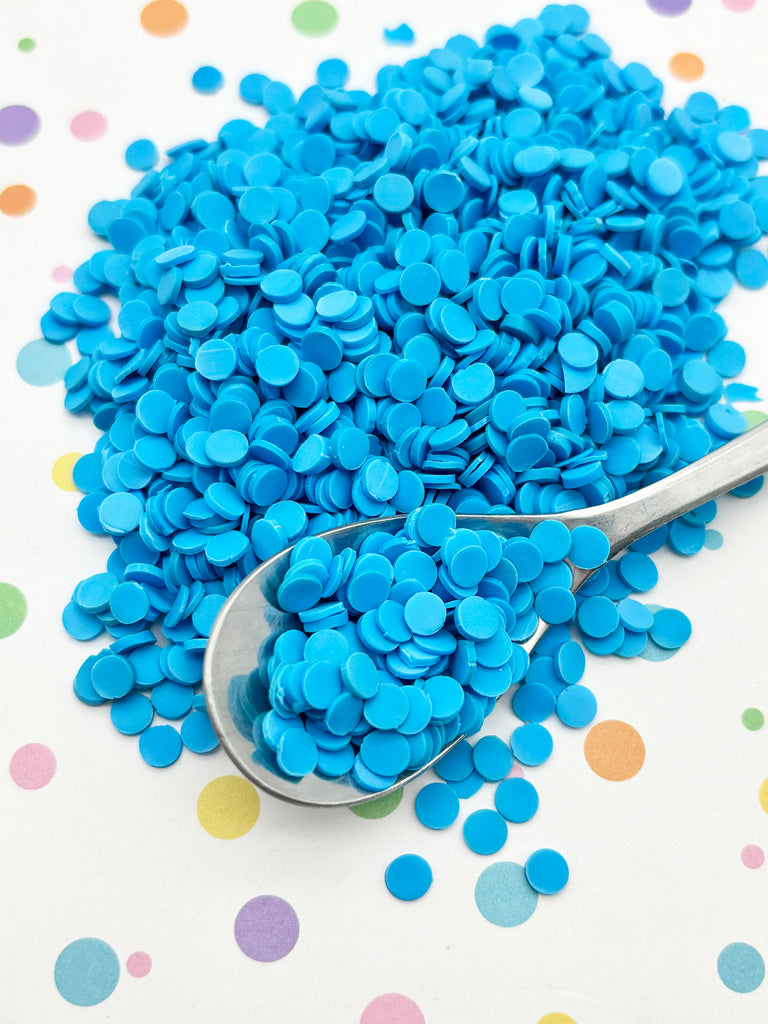 a pile of blue confetti-like objects on a white background, with a spoon partially submerged in the pile.