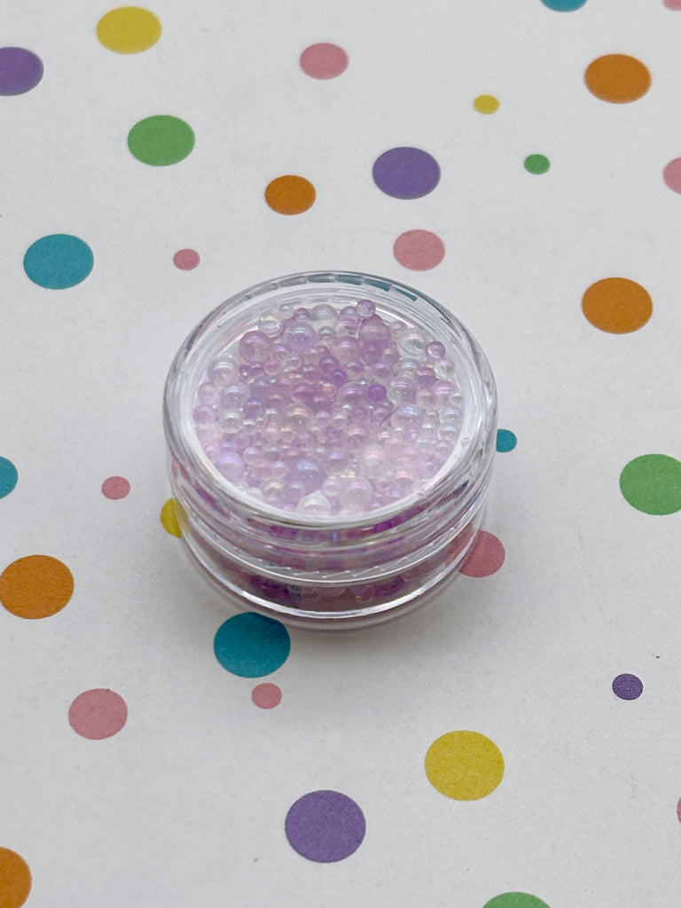 A small glass container filled with purple beads is placed on a white surface with colorful polka dots.