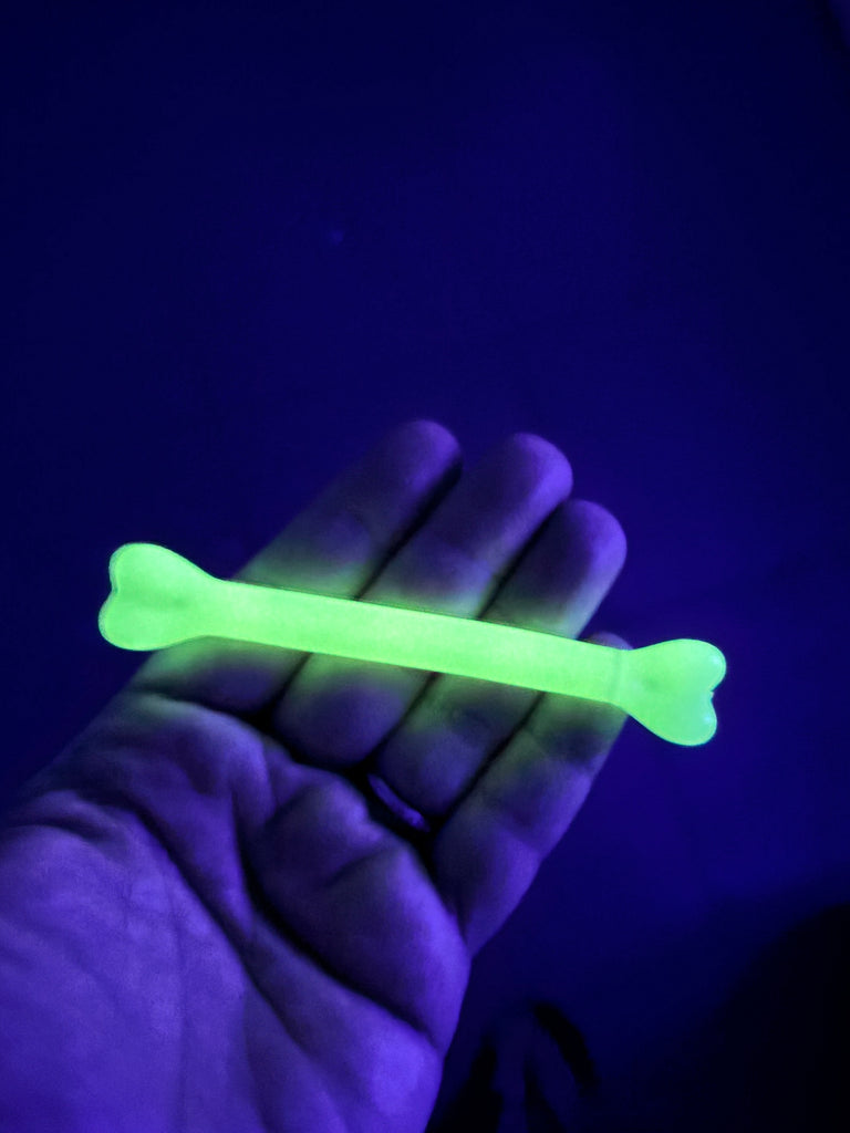 A hand holding a glowing green bone-shaped object against a dark blue background.
