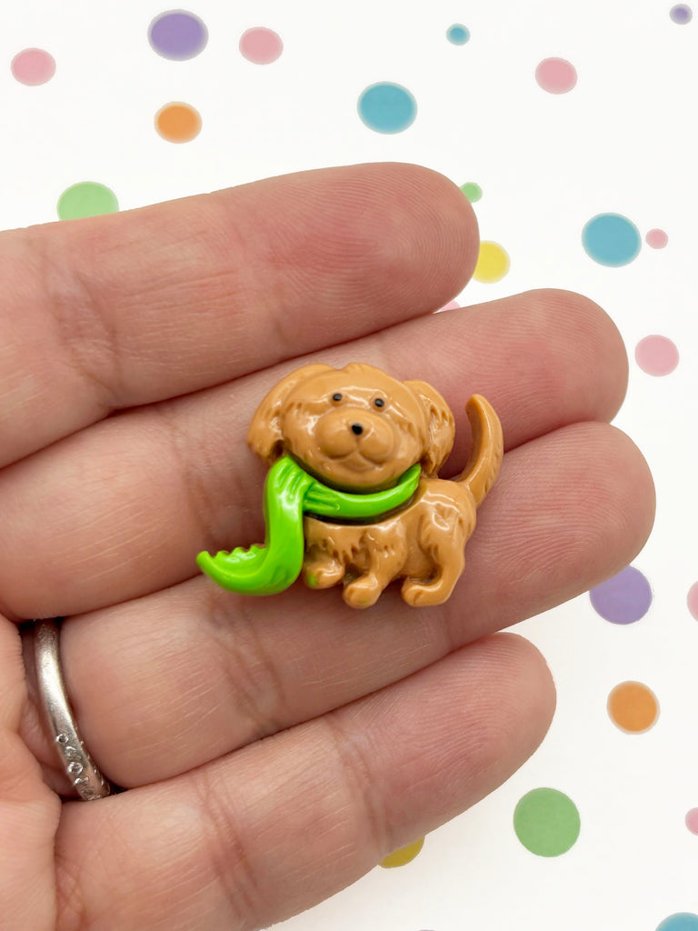 A hand holding a small toy dog with a green scarf around its neck.