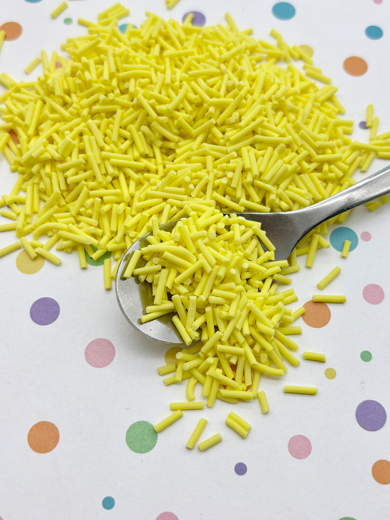 a pile of yellow sprinkles on a white surface with colorful polka dots. A spoon is visible, and the sprinkles are scattered around it.